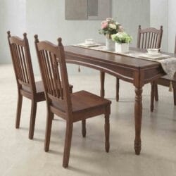 Close-up perspective view of a Casa Furnishing premium solid wood dining table set, showcasing elegant vertical slatted-back wooden chairs and a polished rectangular table adorned with a classic tasseled runner and floral centerpieces.