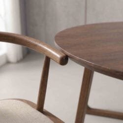 Close-up detail of the smooth polished finish, curved armrest, and fine joinery on a premium wooden dining chair and table.