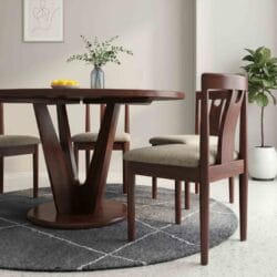 Elegant round solid wood dining table set with four upholstered wooden chairs arranged on a circular grey area rug.