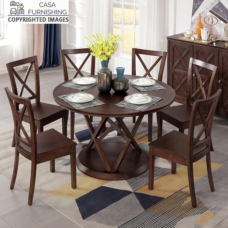 6-seater-round-dining-table-2-1-1-1.jpg Round solid wood dining table set with 6 cross-back chairs in a dark walnut finish by Casa Furnishing, featuring a unique geometric pedestal base.