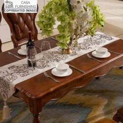 Close-up of an ornate solid wood dining table with scalloped edges and a rich dark finish, styled with a decorative runner and floral centerpiece by Casa Furnishing.