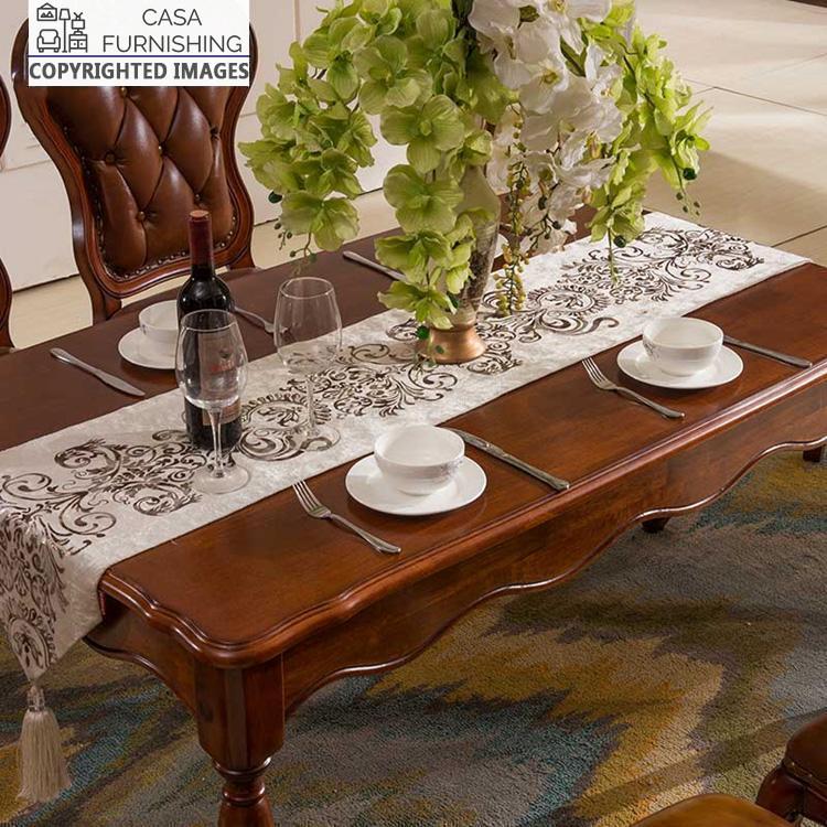 dining-room-sets-2-1-1-1-1.jpg Close-up of an ornate solid wood dining table with scalloped edges and a rich dark finish, styled with a decorative runner and floral centerpiece by Casa Furnishing.